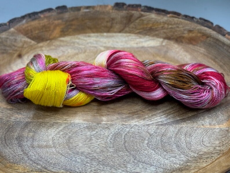 May include: A skein of yarn in shades of pink, brown, yellow, and white. The yarn is twisted and knotted, creating a textured look.
