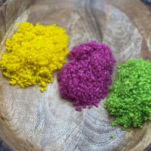 Può includere: Tre mucchi di filato colorato in una ciotola di legno. Il filato è giallo, rosa e verde.