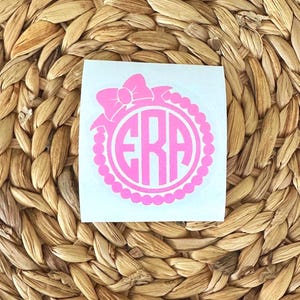 K&ouml;nnte beinhalten: Rosafarbener Monogramm-Aufkleber mit Schleife und Perlenrand. Das Monogramm besteht aus den Buchstaben "ERA".