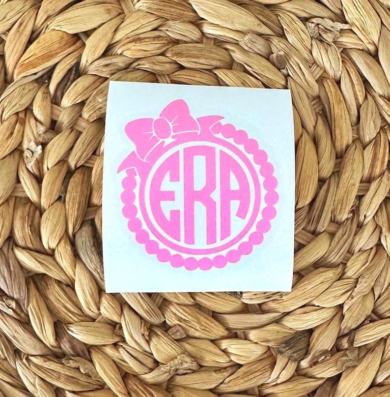 K&ouml;nnte beinhalten: Rosafarbener Monogramm-Aufkleber mit Schleife und Perlenrand. Das Monogramm besteht aus den Buchstaben "ERA".