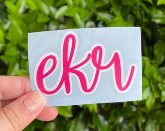 May include: Pink vinyl sticker with the word "ekr" written in a cursive font.