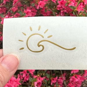 May include: A gold sun and wave design on a white background. The sun has rays and the wave is stylized.