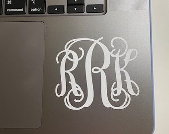 May include: A white monogram sticker with the letters "RRK" in a cursive font on a silver laptop.