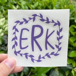 May include: Purple vinyl sticker with a wreath of leaves surrounding the word "ERK" in a handwritten font.