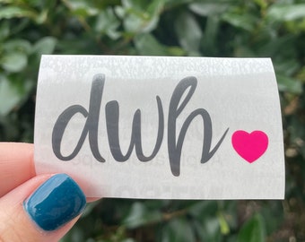 May include: A white sticker with the word "duh" written in black cursive lettering and a pink heart to the right of the word.