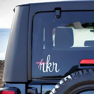May include: A black Jeep with a white vinyl decal that says "rkr" with a pink bow on the "r".