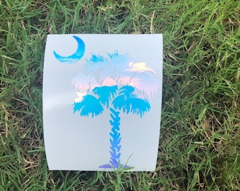 Op de afbeelding: Een blauwe en paarse, iriserende vinyl sticker van een palmboom met een halve maan. De sticker is op een witte achtergrond.