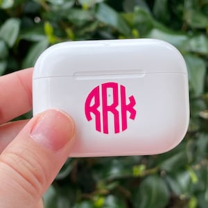 May include: White wireless charging case with a pink monogram sticker that says "RRK" on the front.