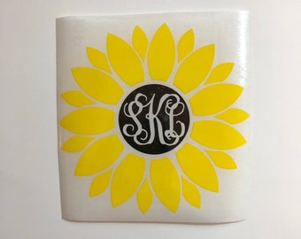 May include: A yellow sunflower with a black circle in the center. The circle has white letters inside that spell "SKI".