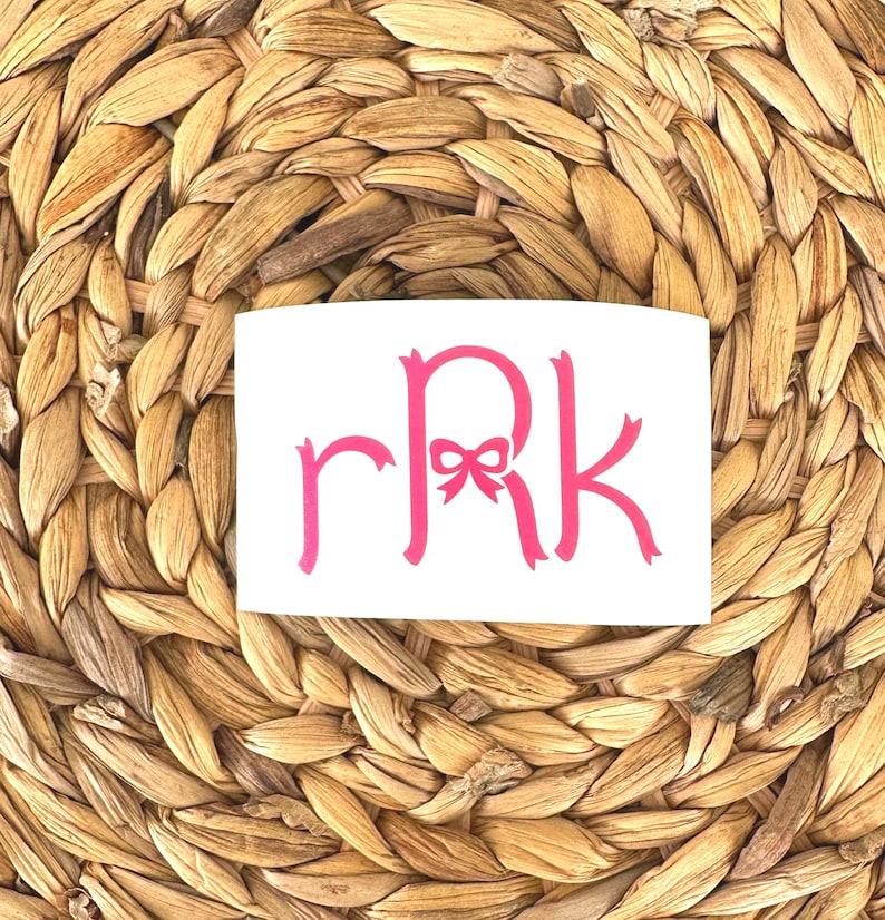K&ouml;nnte beinhalten: Ein wei&szlig;er Aufkleber mit einem rosafarbenen Monogramm "RRK" mit einer rosafarbenen Schleife in der Mitte des "R".