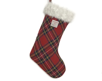 May include: A red Christmas stocking featuring a classic plaid pattern in yellow, black, and white lines. The stocking has a white faux fur cuff at the top and a matching plaid hanging loop. A small white rectangular label reads Harris Tweed.