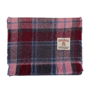 May include: A folded Harris Tweed blanket featuring a plaid design in pink, burgundy, grey, and light blue. The blanket has a fringed edge and a label that reads "Harris Tweed".