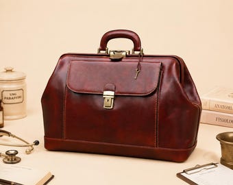 May include: A burgundy leather doctor's bag with a handle, front pocket, and brass hardware. A small key hangs from the lock. Medical equipment, including a stethoscope, jars, and books, are arranged around the bag.