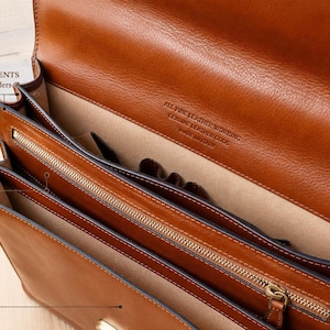 Pu&ograve; includere: Una cartella in pelle color cuoio con due scomparti principali dotati di portacarte e portapenne, una tasca centrale con cerniera e due ampie tasche frontali. L'interno &egrave; foderato in tessuto beige e la pelle reca l'incisione All Fine Leather Working, Genuine Leather Code, Made in Italy.