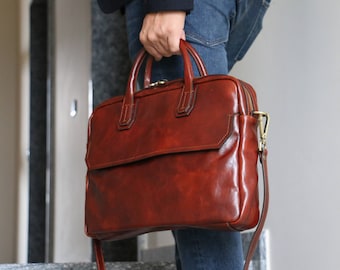 May include: A brown leather briefcase with a gold zipper and a strap. The briefcase has a flap with a buckle closure.