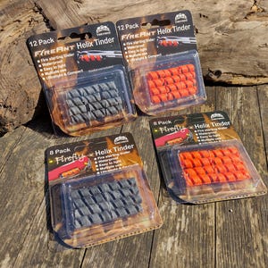 May include: Four packs of Firefly Helix Tinder fire starters. Two packs are labelled "12 Pack" and contain grey tinder. The other two packs are labelled "8 Pack" and contain orange tinder. The packaging is clear plastic.
