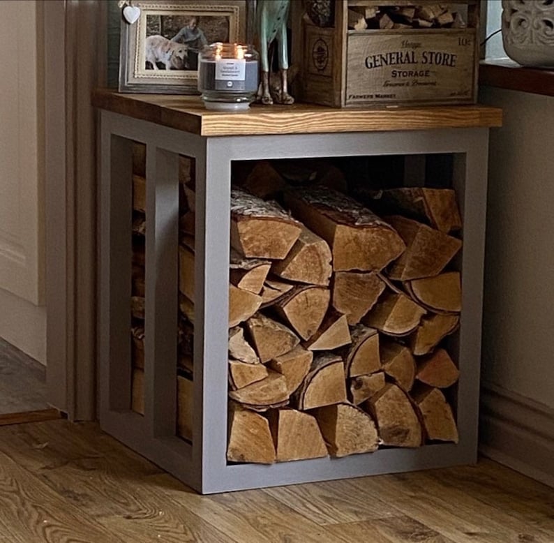 May include: A gray metal log rack with a wooden top. The rack is filled with stacked firewood.