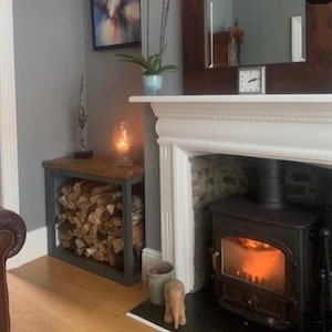 May include: A white fireplace with a black wood-burning stove. The stove has a glass door and a glowing fire inside. There is a wooden log rack next to the fireplace.