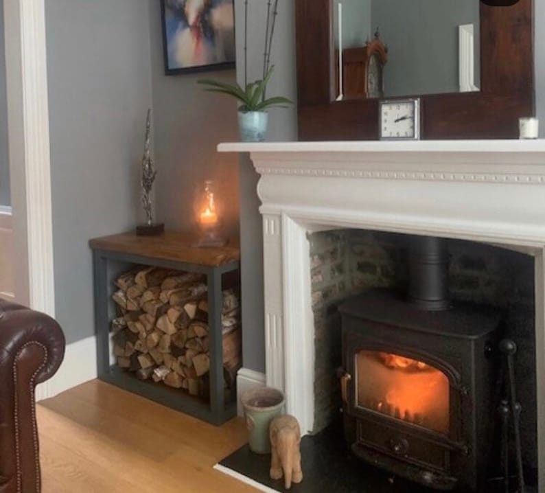 May include: A white fireplace with a black wood-burning stove. The stove has a glass door and a glowing fire inside. There is a wooden log rack next to the fireplace.