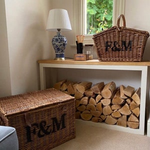 May include: Two wicker baskets with the letters "F&M" on them. The baskets are sitting on a white shelf with a stack of firewood behind them. A lamp with a white shade and a blue and white ceramic base is on the shelf above the baskets.