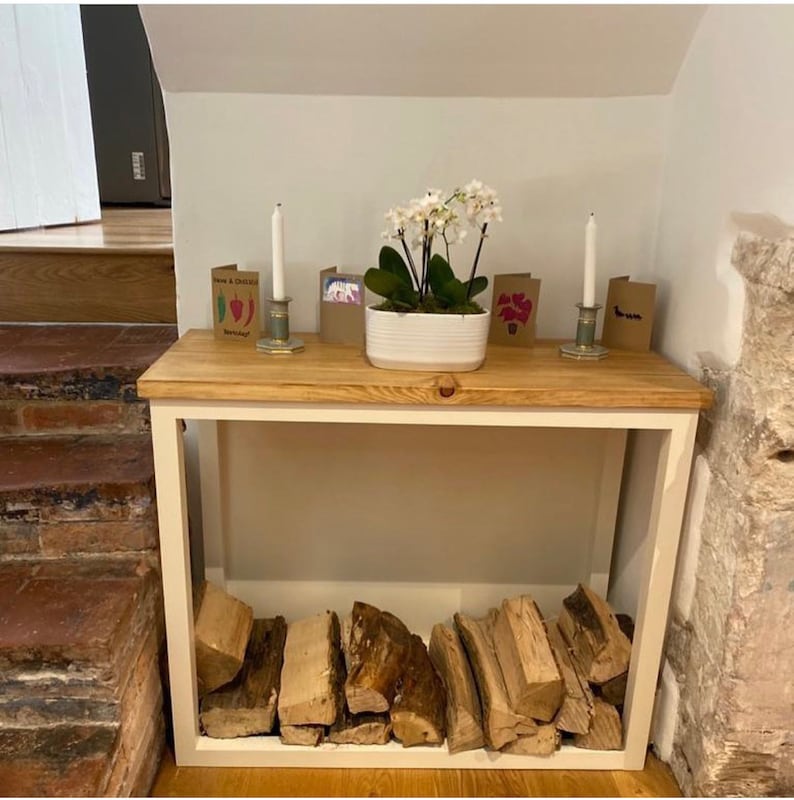 May include: A white wood console table with a wooden top and a white metal frame. The table has a shelf underneath for storage. There are candles and a potted white orchid on the top of the table. There are also some cards on the table.