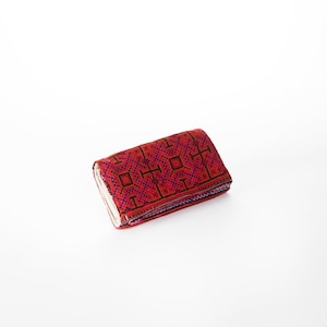 May include: A red and black patterned wallet with a geometric design. The wallet is folded closed and is sitting on a white surface.