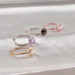 Puede incluir: Cuatro anillos envueltos en alambre con piedras preciosas de diferentes colores. Los anillos est&aacute;n hechos de alambre de plata y oro. Las piedras preciosas son rosas, negras, moradas y transparentes.