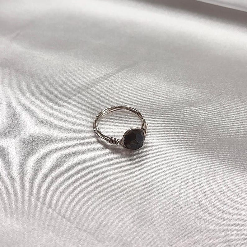 Puede incluir: Un anillo de plata con una piedra preciosa gris oscuro engastada en el centro.