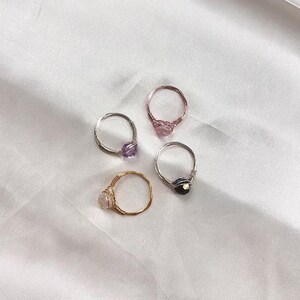 Puede incluir: Cuatro anillos envueltos en alambre con piedras preciosas de diferentes colores. Los anillos est&aacute;n hechos de alambre de plata y oro. Las piedras preciosas son moradas, rosas, negras y transparentes.