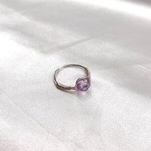 Puede incluir: Un anillo de alambre plateado con una piedra preciosa de amatista p&uacute;rpura.