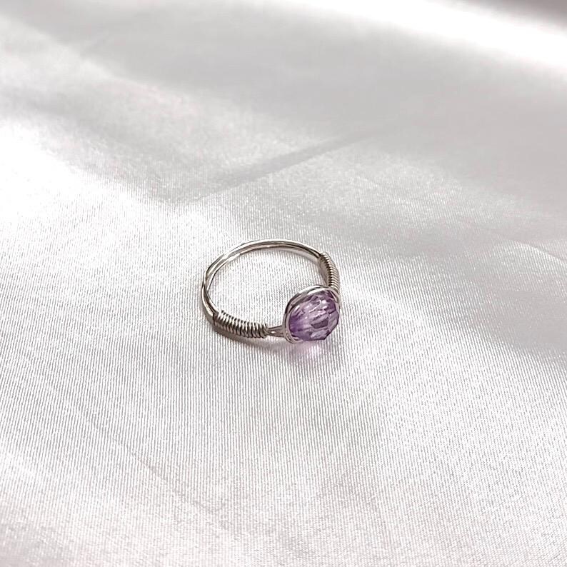 Puede incluir: Un anillo de alambre plateado con una piedra preciosa de amatista p&uacute;rpura.