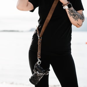 May include: A person wearing black clothing with a brown leather camera strap and a camera attached to the strap.