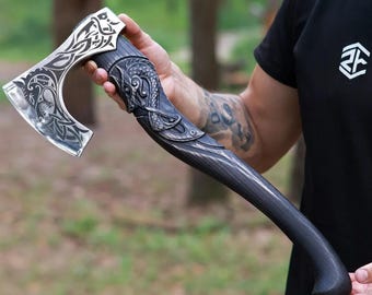 May include: A hand holds a black-handled axe with a silver blade. The blade is decorated with intricate carvings of a dragon and other designs.