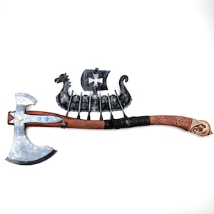 May include: A wooden-handled axe with a black metal head and a blue and silver design. The axe head features a Viking ship with a cross on the sail.