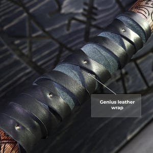 May include: Close-up of a wooden handle with a black leather wrap. The leather is wrapped in a spiral pattern and secured with small metal studs. The text "Genius leather wrap" is visible.