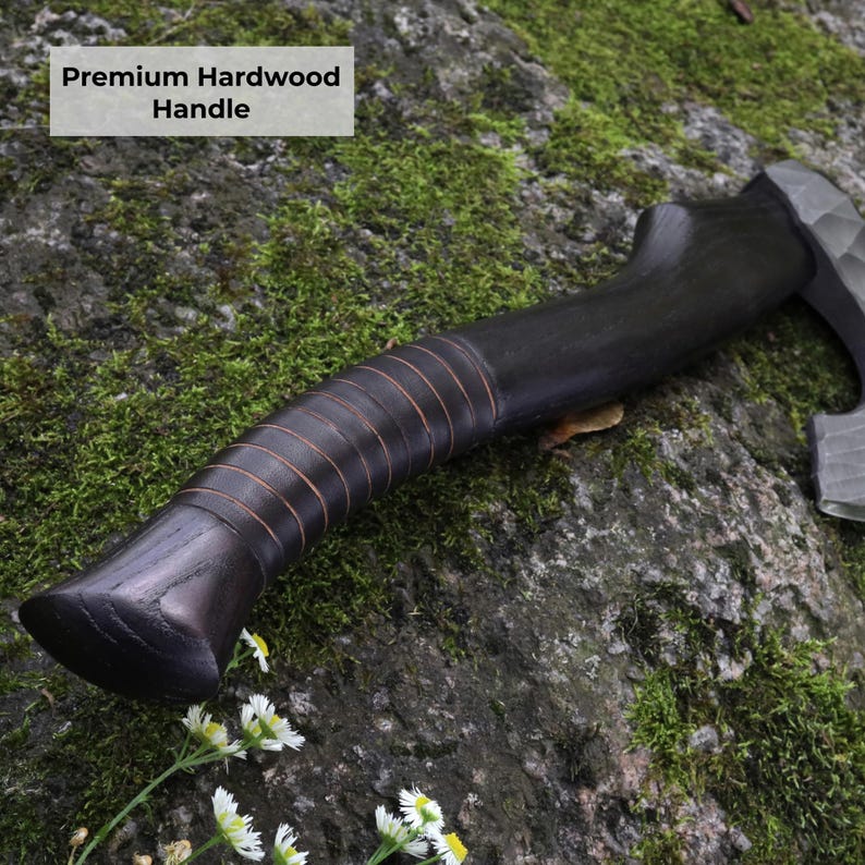 May include: A dark-stained hardwood axe handle featuring a series of carved horizontal grooves along the grip. The handle is curved and smooth, with the text Premium Hardwood Handle visible in the upper left corner of the image.