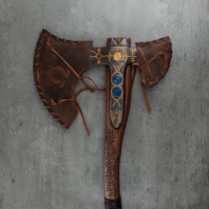May include: A double-bitted axe featuring a dark brown wooden handle with intricate carvings, a metal head with gold-colored geometric engravings, two circular blue inlays, and brown leather covers laced onto the blades with leather cords.