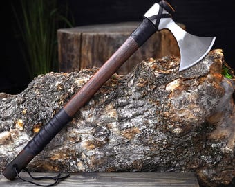 Peut inclure: Une hache artisanale avec une lame en acier poli et un manche en bois foncé. La poignée est enveloppée de cuir noir pour une meilleure prise. La hache est présentée sur une bûche texturée et vieillie, mettant en valeur son design rustique.