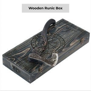May include: A black axe with a wooden handle and intricate carvings is displayed in a wooden box with a runic design. The box is labeled "Wooden Runic Box".