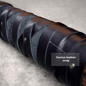 May include: A cylindrical object featuring a black leather wrap applied in a crisscross pattern. The leather strips are secured with small brass-colored metal rivets. A text overlay on the image reads, Genius leather wrap, with a line pointing to the wrap.