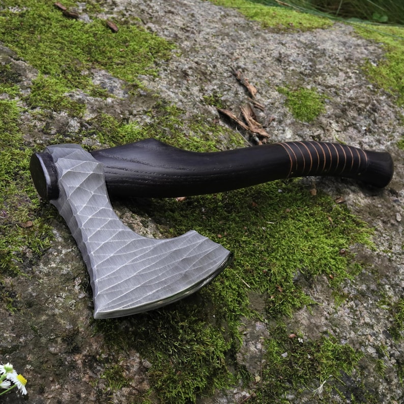 May include: A hand axe featuring a silver-colored metal head with a distinct diamond-patterned, faceted texture. The handle is crafted from dark, stained wood and includes a series of thin, copper-colored wire wraps near the grip area.