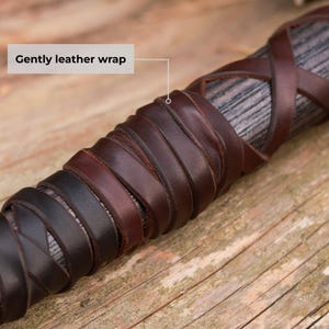 May include: Close-up of a wooden handle wrapped in dark brown and black leather. The leather is intricately woven and appears to be hand-stitched. The text "Gently leather wrap" is in the image.
