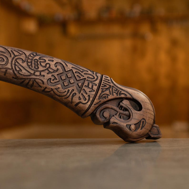 May include: A dark brown wooden handle featuring intricate carved patterns and a stylized animal head at the pommel. The surface displays deep, etched geometric lines and swirling motifs that cover the length of the grip, ending in a sculpted creature.