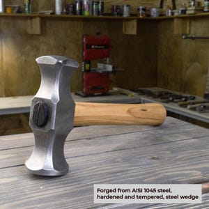 K&ouml;nnte beinhalten: Ein Stahlkeilhammer mit Holzgriff. Der Hammerkopf ist aus AISI 1045 Stahl geschmiedet und hat eine strukturierte, graue Oberfl&auml;che. Der Griff ist aus hellem Holz gefertigt. Der Text auf dem Bild lautet: "Geschmiedet aus AISI 1045 Stahl, geh&auml;rtet und verg&uuml;tet, Stahlkeil."