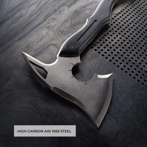 Puede incluir: Un hacha de acero con alto contenido de carbono con un mango negro y un dise&ntilde;o de hoja &uacute;nico. El cabezal del hacha presenta un recorte circular y un filo afilado. El texto "HIGH-CARBON AISI 1065 STEEL" est&aacute; visible.
