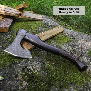 May include: A hand axe with a textured, dark grey metal head and a smooth, dark brown wooden handle wrapped with thin leather cord. The axe head features a curved, sharpened edge. The text "Functional Axe &ndash; Ready to Split" is visible.
