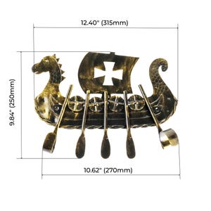 May include: A gold and black metal wall art piece shaped like a Viking ship with a sail featuring a cross cutout. The ship includes four oars and measures 12.40 inches wide by 9.84 inches high, with a base width of 10.62 inches as indicated.