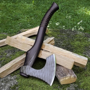 May include: A hand axe featuring a dark brown wooden handle with a series of horizontal grooves and a silver-colored metal head with a textured, faceted surface pattern. The axe head has a curved blade edge and a distinct, geometric design.