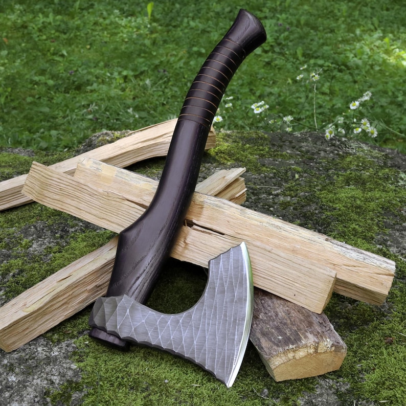 May include: A hand axe featuring a dark brown wooden handle with a series of horizontal grooves and a silver-colored metal head with a textured, faceted surface pattern. The axe head has a curved blade edge and a distinct, geometric design.