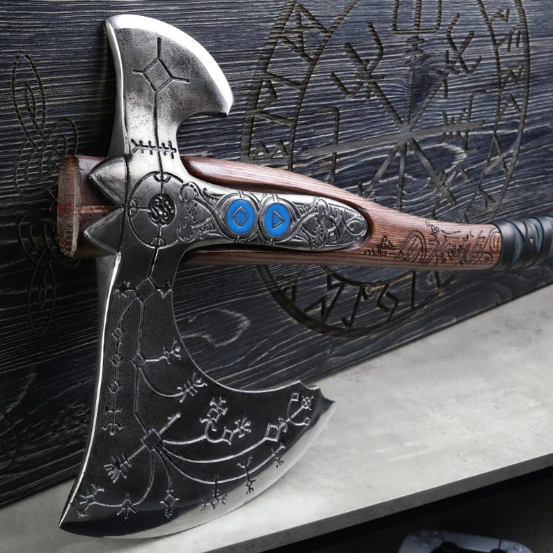 May include: A detailed, silver-colored axe with intricate engravings and a wooden handle. The handle features blue accents and decorative metalwork. The axe is mounted on a dark wooden surface with carved symbols, showcasing a blend of craftsmanship and design.